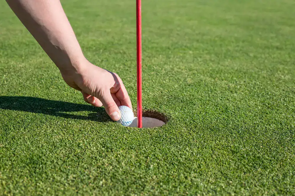 Player carefully putting their golf ball across a wooden rope bridge obstacle
